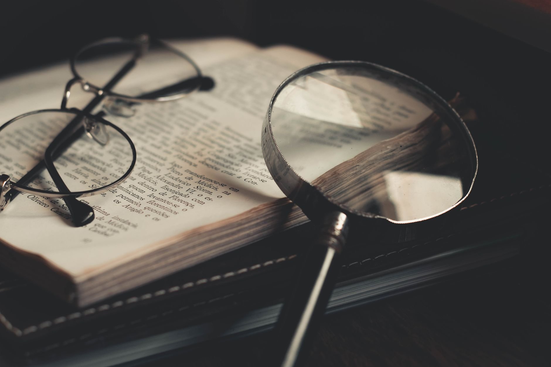 Close-up of an open reference book with a magnifying glass, representing research and discovery.