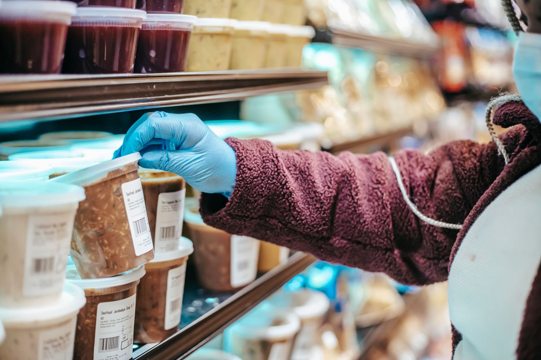A person carefully reading the label on a frozen food container at a grocery store.